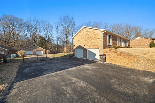 view of home's exterior featuring brick siding, fence, driveway, and an attached garage