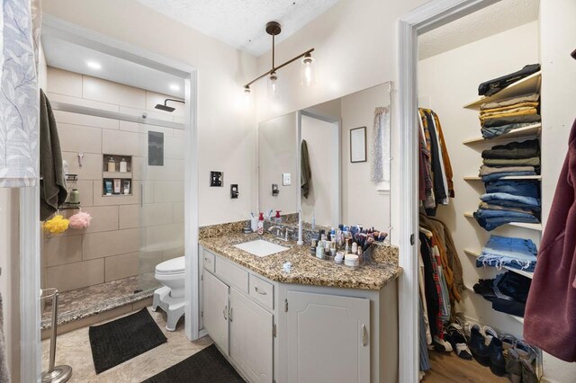 full bathroom featuring a walk in closet, tiled shower, vanity, and toilet