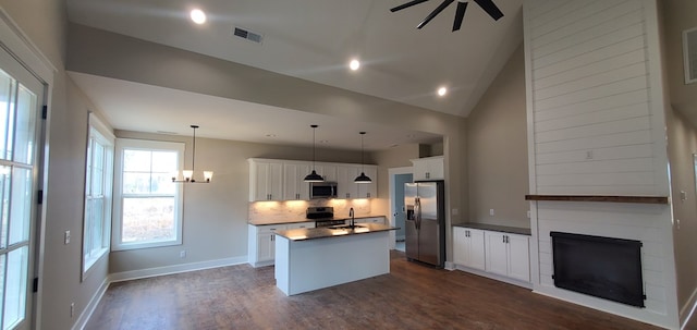 kitchen featuring a center island with sink, white cabinets, dark countertops, decorative light fixtures, and stainless steel appliances