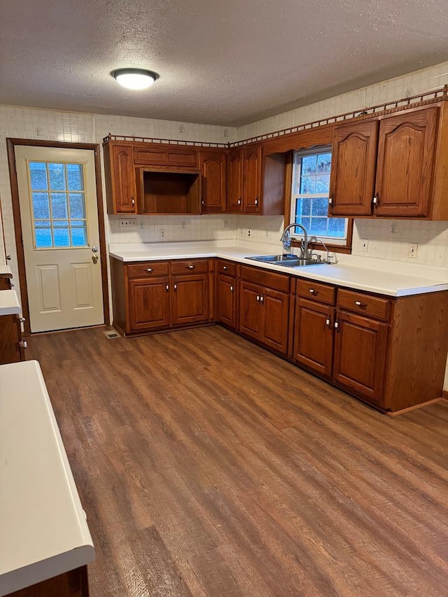 kitchen with tasteful backsplash, brown cabinets, dark wood-type flooring, light countertops, and a sink