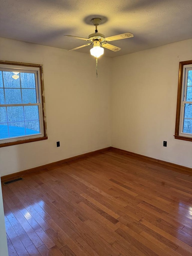 unfurnished room featuring a wealth of natural light, visible vents, baseboards, and wood finished floors