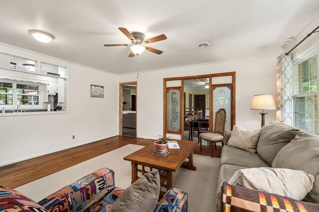 living room with visible vents, baseboards, ceiling fan, ornamental molding, and wood finished floors