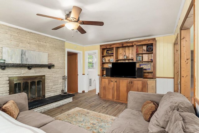 living area with light wood finished floors, ceiling fan, a fireplace, and crown molding