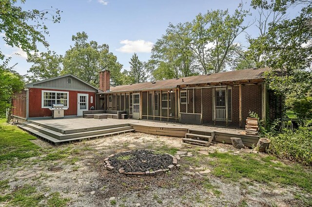 back of house with brick siding, a chimney, a sunroom, and a wooden deck