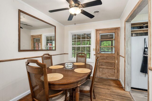 dining room featuring a wainscoted wall, crown molding, visible vents, a ceiling fan, and wood finished floors