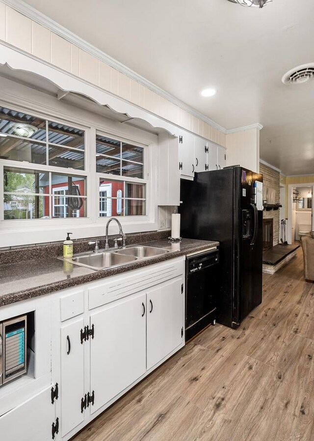 kitchen with dark countertops, ornamental molding, white cabinetry, a sink, and black appliances