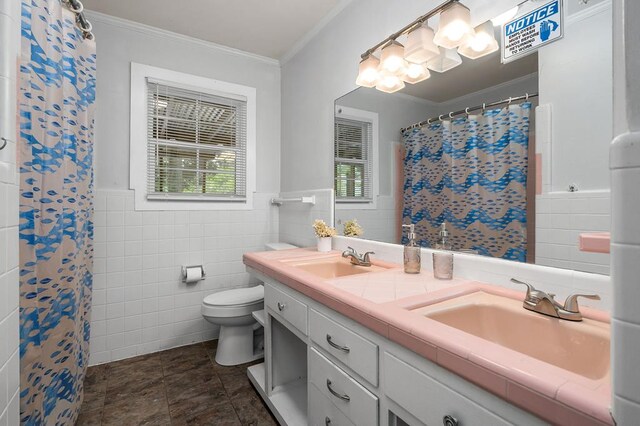 bathroom with double vanity, crown molding, tile walls, and a sink