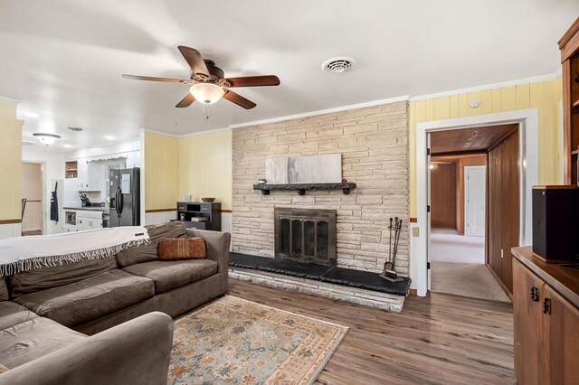 living area featuring visible vents, ceiling fan, crown molding, light wood-style floors, and a fireplace