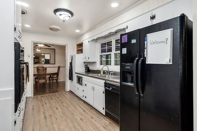 kitchen with white cabinets, dark countertops, light wood-style flooring, black appliances, and a sink