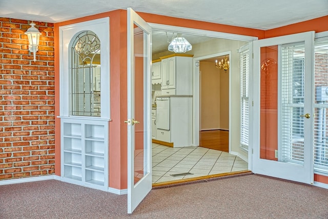 foyer featuring light carpet, a notable chandelier, brick wall, and baseboards