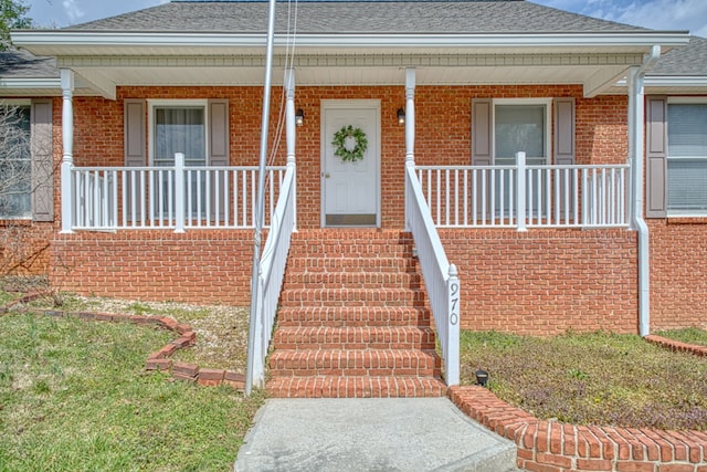 property entrance featuring brick siding, covered porch, and a shingled roof