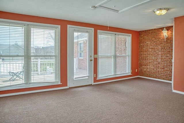 unfurnished room featuring brick wall, attic access, baseboards, and carpet floors