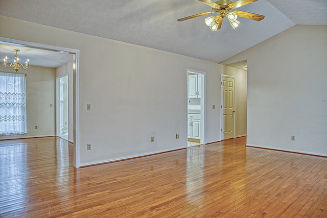 empty room featuring ceiling fan with notable chandelier, light wood-type flooring, baseboards, and vaulted ceiling