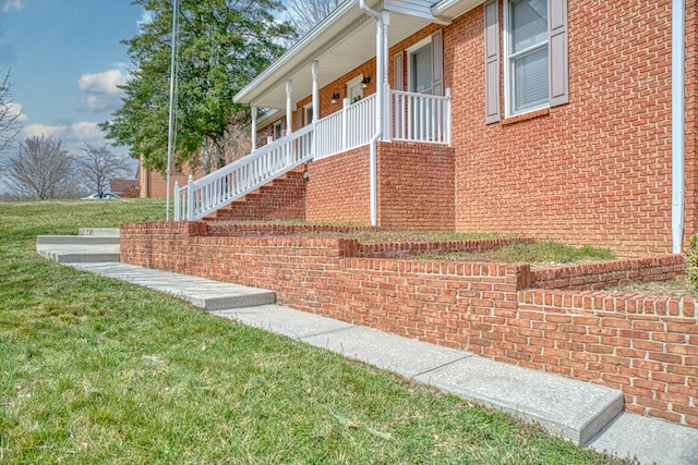 view of side of property featuring brick siding, covered porch, and a yard