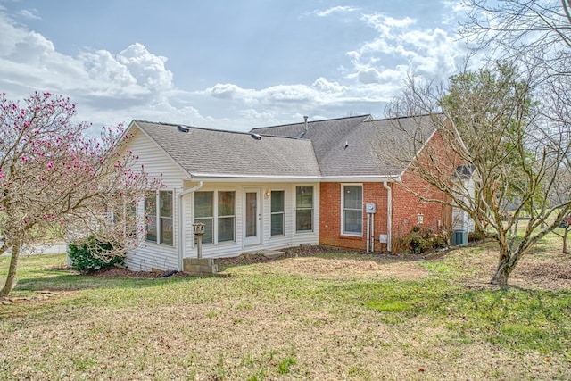 rear view of property with cooling unit, a lawn, brick siding, and a shingled roof