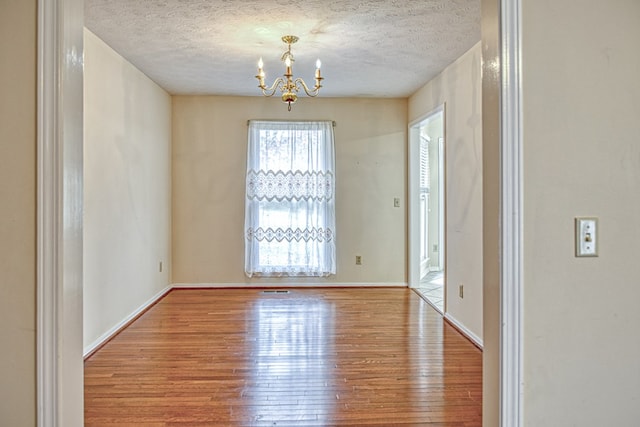 unfurnished room with a notable chandelier, a textured ceiling, baseboards, and wood-type flooring