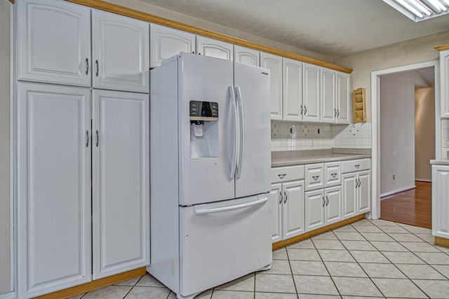 kitchen with light countertops, decorative backsplash, white fridge with ice dispenser, light tile patterned flooring, and white cabinets