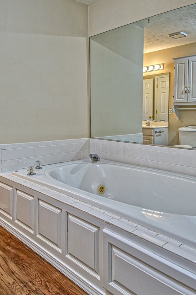 full bathroom with toilet, a tub with jets, wood finished floors, and vanity