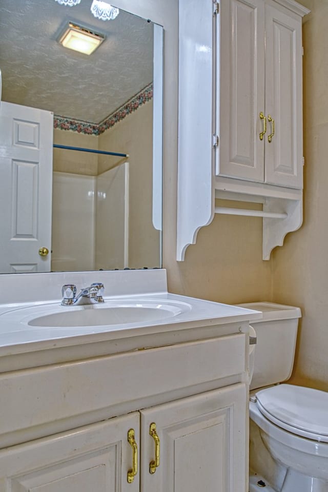 full bath featuring a textured ceiling, toilet, vanity, and walk in shower