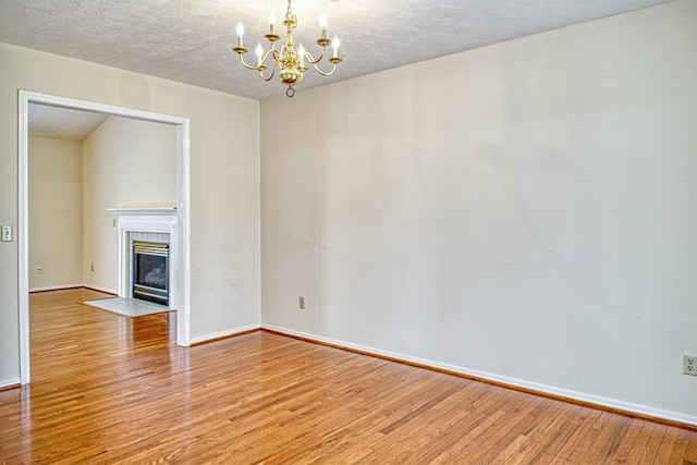 unfurnished room with baseboards, a tiled fireplace, an inviting chandelier, wood finished floors, and a textured ceiling