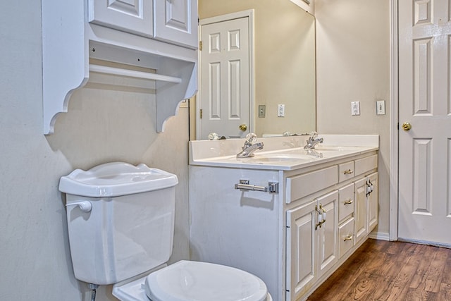 bathroom featuring toilet, a sink, wood finished floors, double vanity, and baseboards