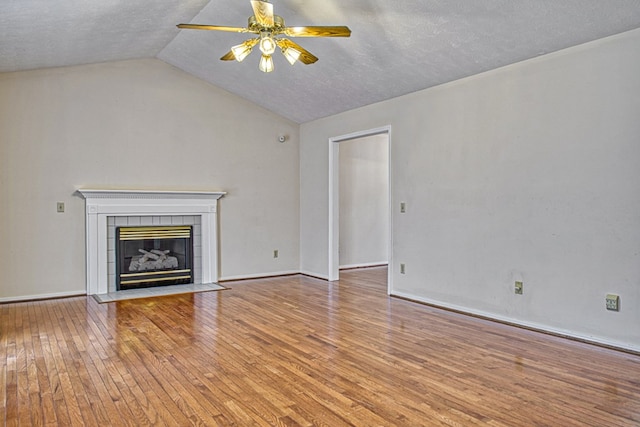 unfurnished living room featuring vaulted ceiling, a tile fireplace, a textured ceiling, a ceiling fan, and wood-type flooring