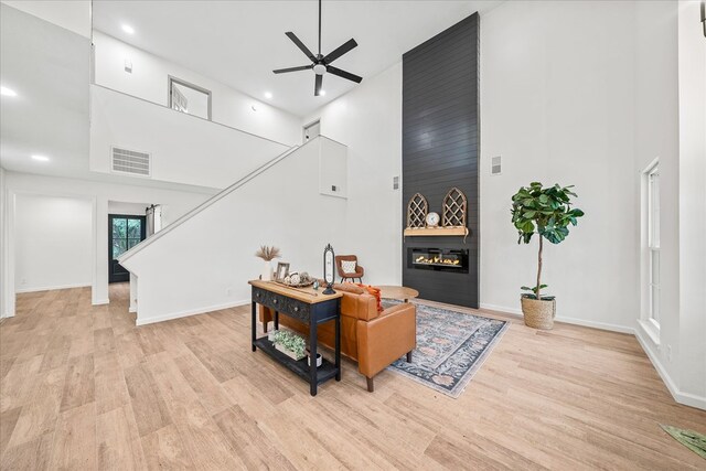 living room with light wood finished floors, a fireplace, a towering ceiling, and a ceiling fan