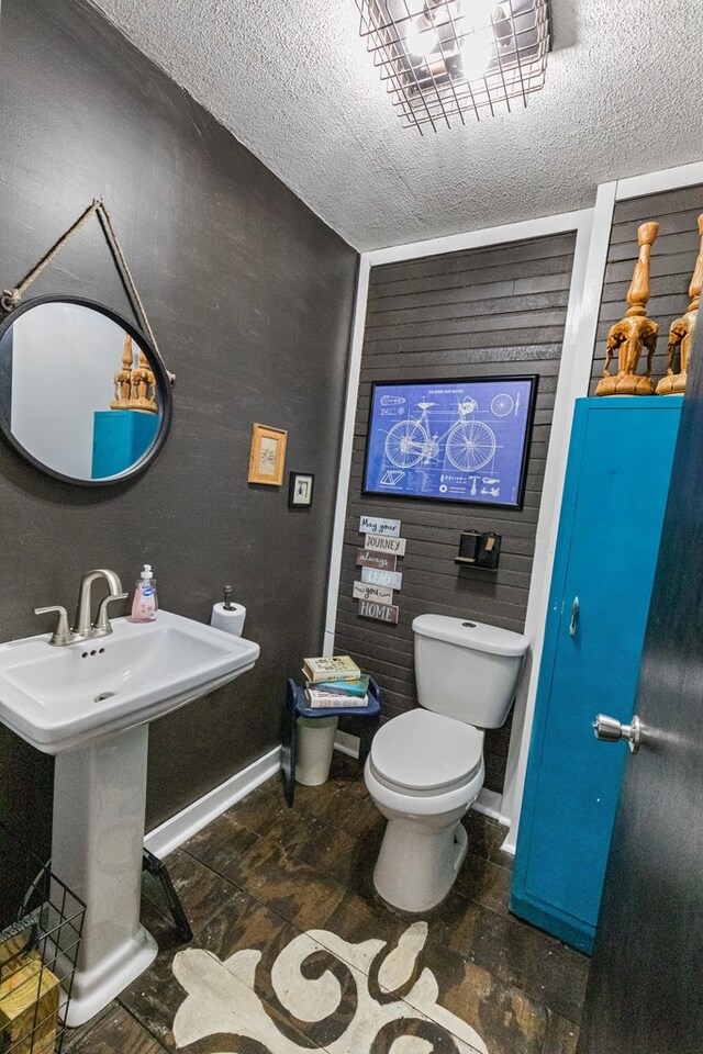 half bath with a textured ceiling, a sink, toilet, and baseboards