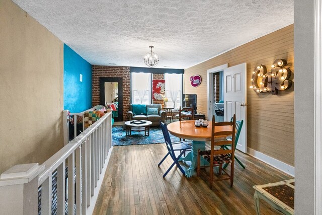 dining space with wooden walls, a textured ceiling, wood finished floors, a chandelier, and baseboards