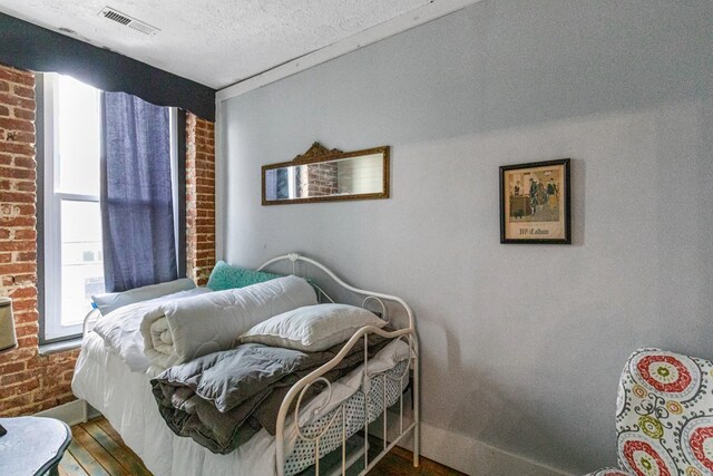 bedroom with a textured ceiling, brick wall, wood finished floors, and visible vents