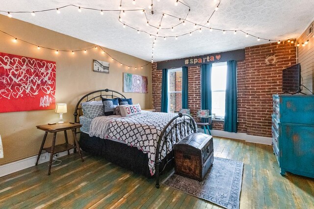 bedroom featuring brick wall, baseboards, dark wood finished floors, and a textured ceiling