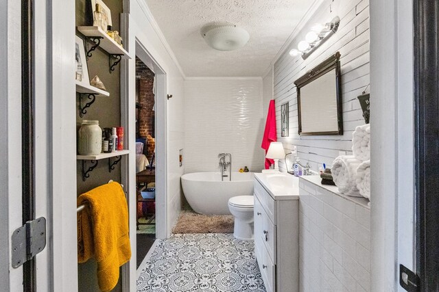 bathroom with a textured ceiling, toilet, vanity, a freestanding bath, and ornamental molding