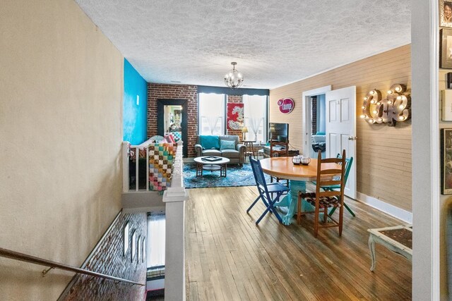 dining space featuring a textured ceiling, wooden walls, wood finished floors, and a notable chandelier