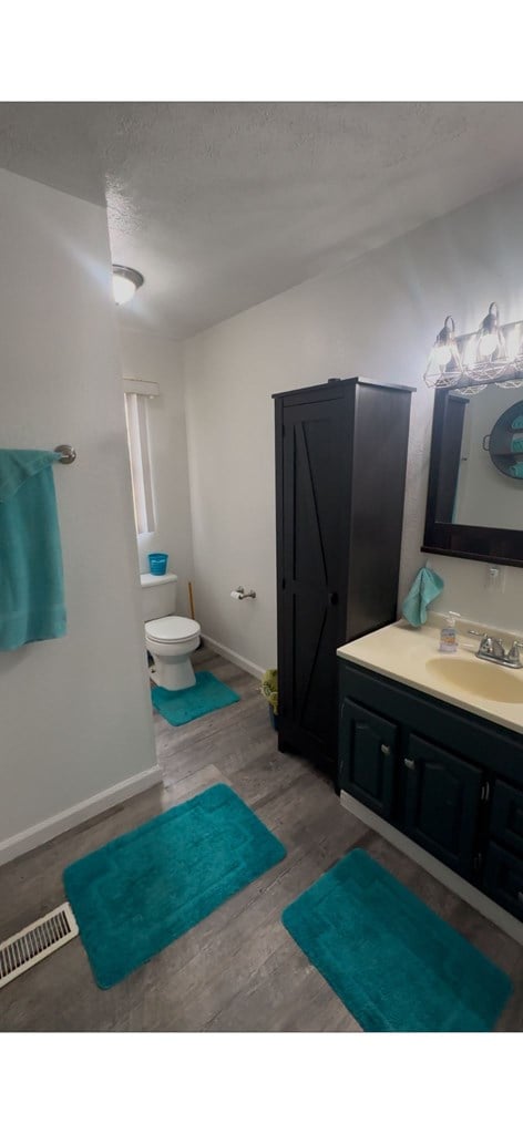 bathroom featuring baseboards, visible vents, toilet, wood finished floors, and vanity