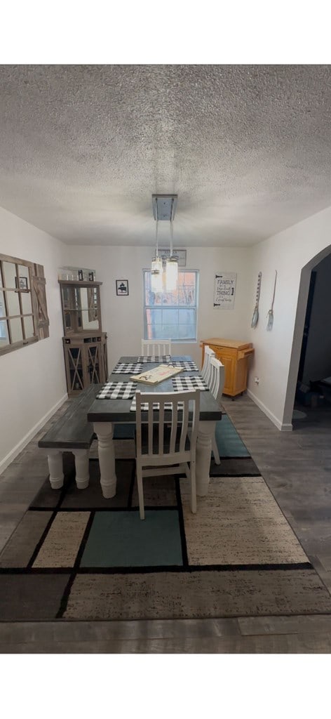 dining area featuring arched walkways, dark wood finished floors, a textured ceiling, and baseboards