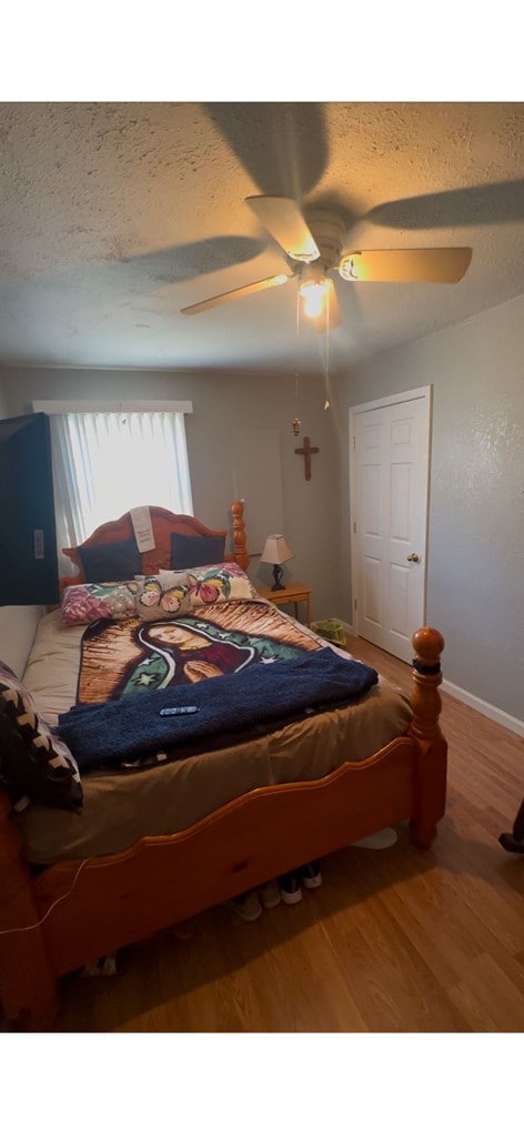 bedroom with a ceiling fan, a textured ceiling, baseboards, and wood finished floors