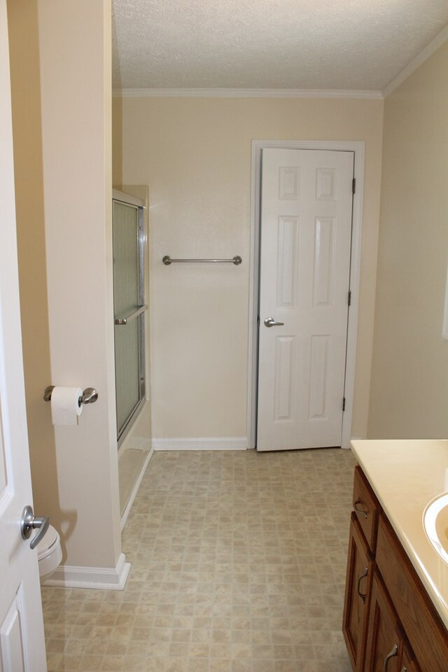 bathroom with toilet, ornamental molding, combined bath / shower with glass door, a textured ceiling, and vanity