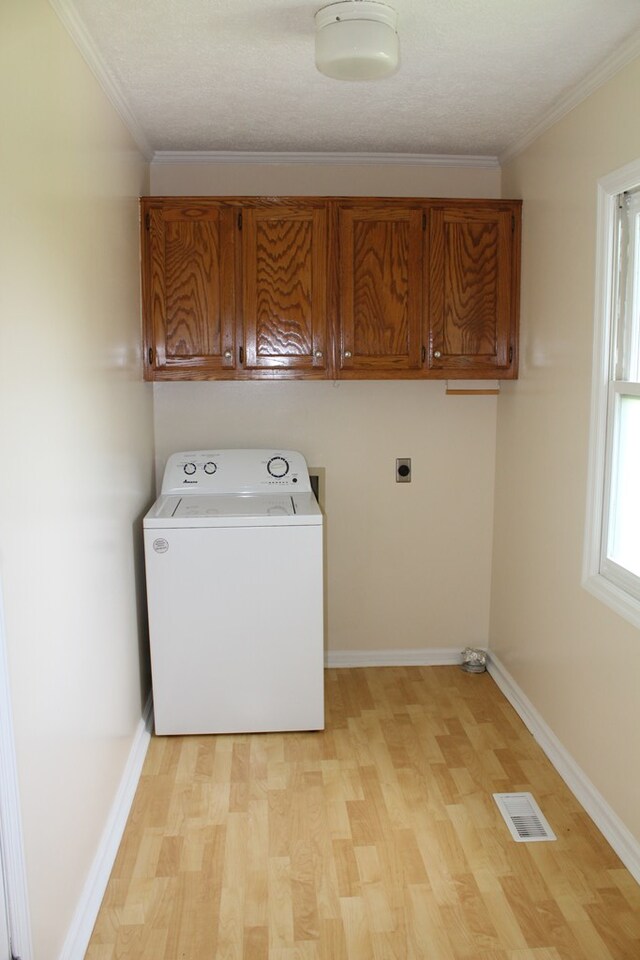 clothes washing area featuring crown molding, cabinet space, visible vents, light wood-style floors, and washer / dryer