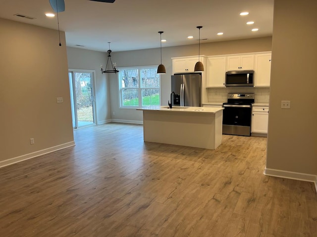 kitchen with stainless steel appliances, white cabinets, hanging light fixtures, light countertops, and an island with sink