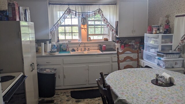 kitchen with wallpapered walls, electric range, light countertops, white cabinetry, and a sink