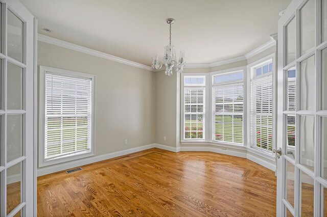 empty room featuring a chandelier, visible vents, crown molding, and wood finished floors