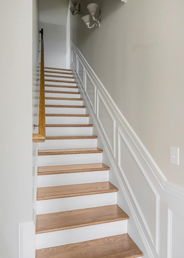 staircase featuring a decorative wall and wainscoting