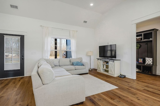 living room featuring visible vents, vaulted ceiling, baseboards, and wood finished floors