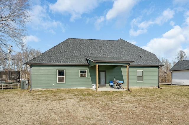 rear view of house featuring roof with shingles, a yard, a trampoline, and a patio area