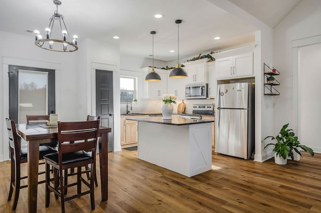 kitchen featuring stainless steel appliances, white cabinets, a center island, dark countertops, and decorative light fixtures