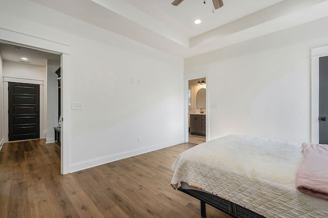 bedroom with dark wood finished floors, recessed lighting, a raised ceiling, ensuite bathroom, and baseboards