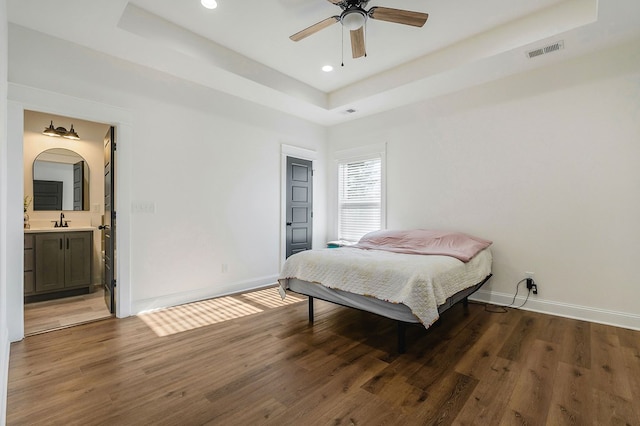 bedroom with a tray ceiling, dark wood-style flooring, visible vents, and a sink