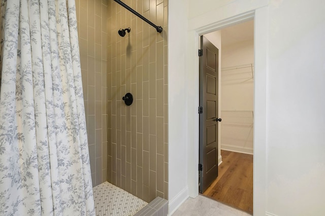 bathroom with wood finished floors, a shower stall, a walk in closet, and baseboards