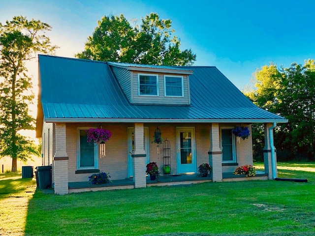 view of front of home featuring a front lawn, brick siding, covered porch, and metal roof