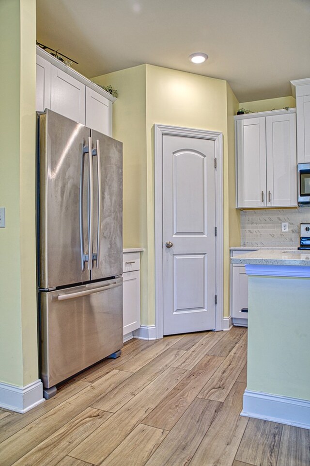 kitchen with light countertops, decorative backsplash, appliances with stainless steel finishes, white cabinets, and light wood-type flooring